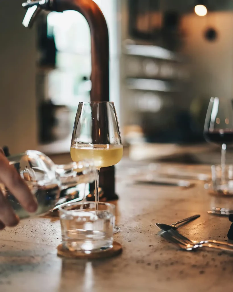 cooking_image_17 Der Privatkoch gießt Wasser in ein Kristallglas. Daneben steht ein Glas voll mit Weißwein. Der Privatkoch bereitet die Getränke vor dem Essen vor.