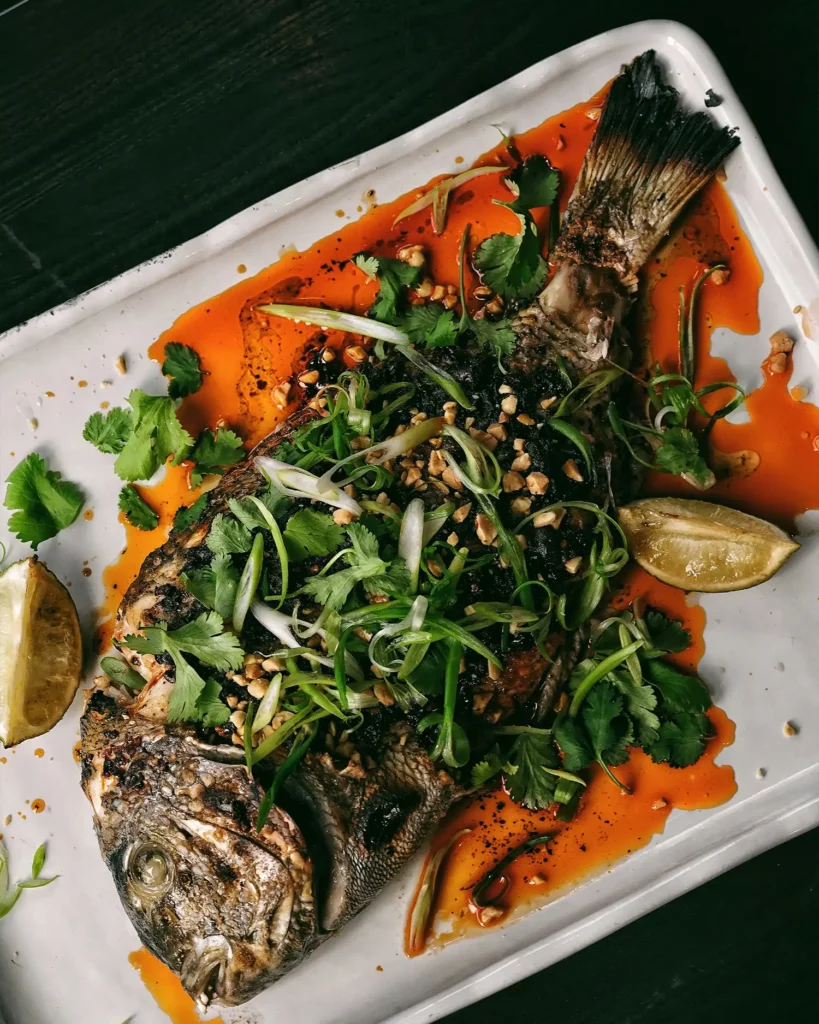 cooking_image_18 Ein wunderschön angerichteter Fisch, zubereitet von einem Privatkoch, garniert mit einer frischen Zitronenscheibe, bereit zum Genießen.
