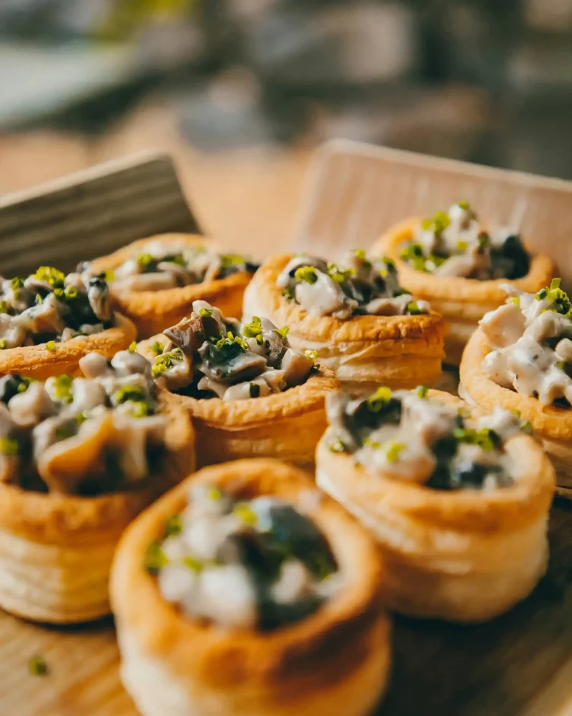 Kleine Blätterteig-Küchlein, gefüllt mit einer herzhaften Mischung aus Pilzen und Käse, goldbraun und appetitlich vom Privatkoch angerichtet.